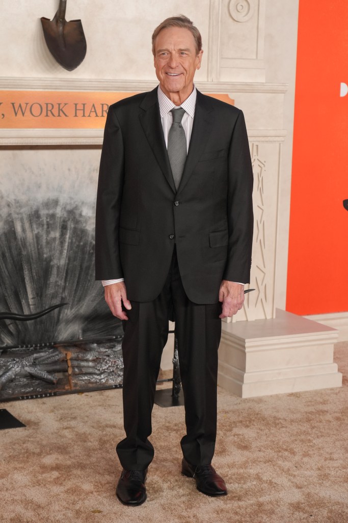 John Goodman in a dark suit and striped shirt.