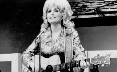 Dolly Parton performs onstage with an acoustic guitar in circa 1974.